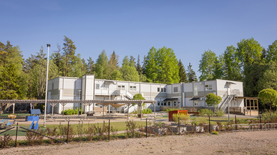 Modulförskola med grön gård och lekutrustning i förgrunden