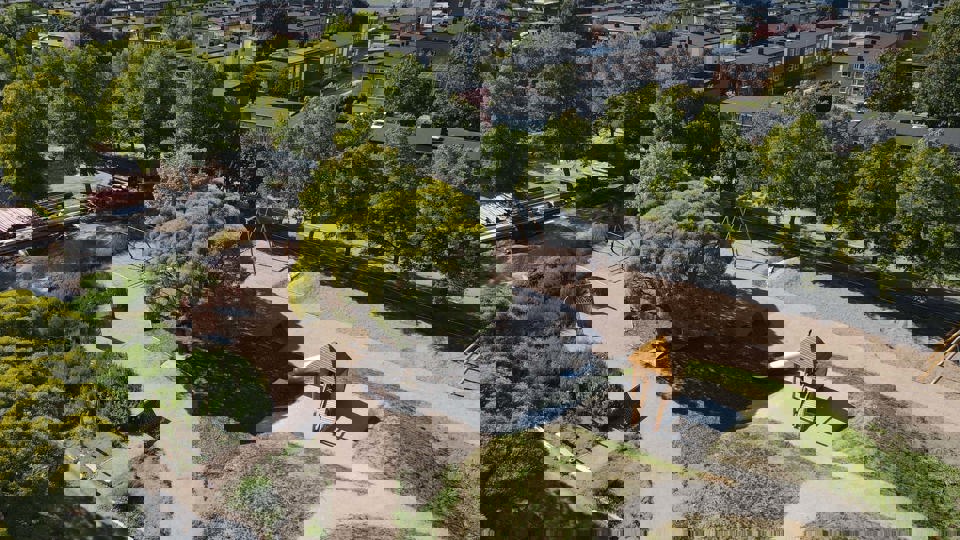 Flygfoto över byggplats där skola med skolgård och gröna träd växer fram .
