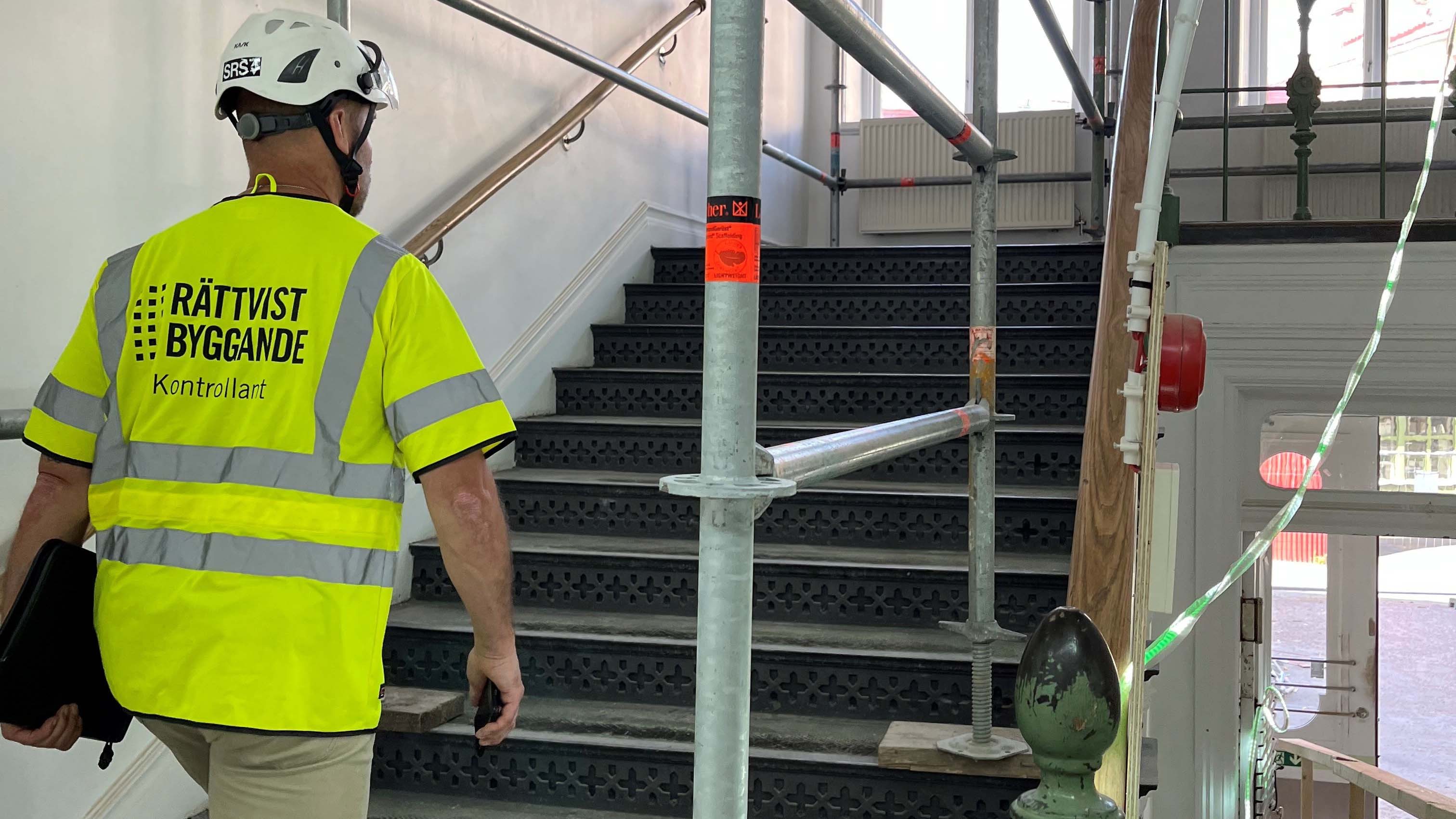 Kontrollant med gul väst och hjälm går uppför en trappa i en byggnad som renoveras