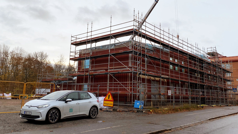 Byggplats där en ny, röd förskola i trä håller på att byggas. 