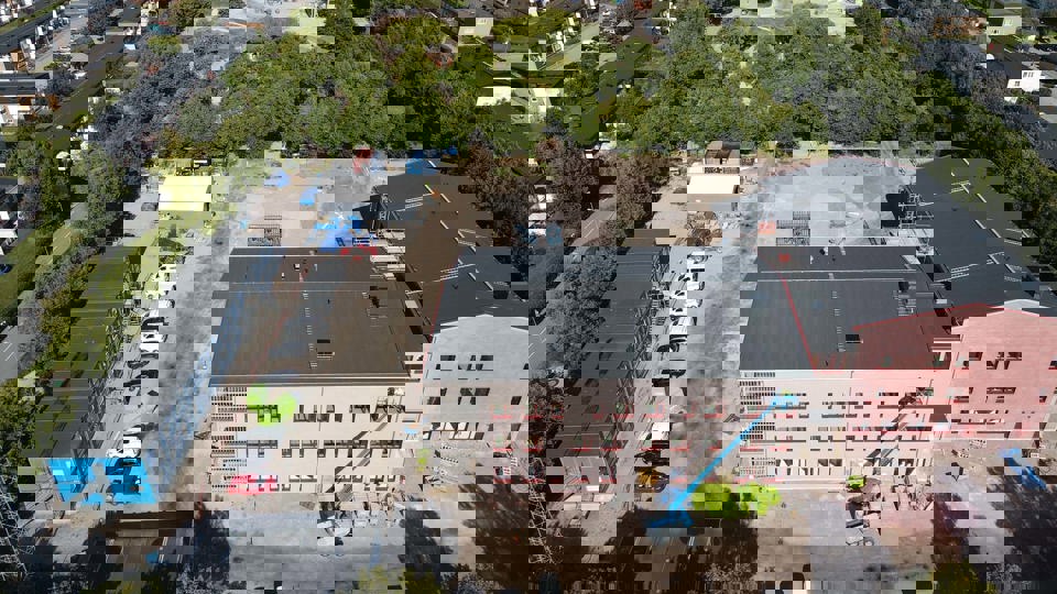 Flygfoto över byggplats där skola med skolgård och gröna träd växer fram .