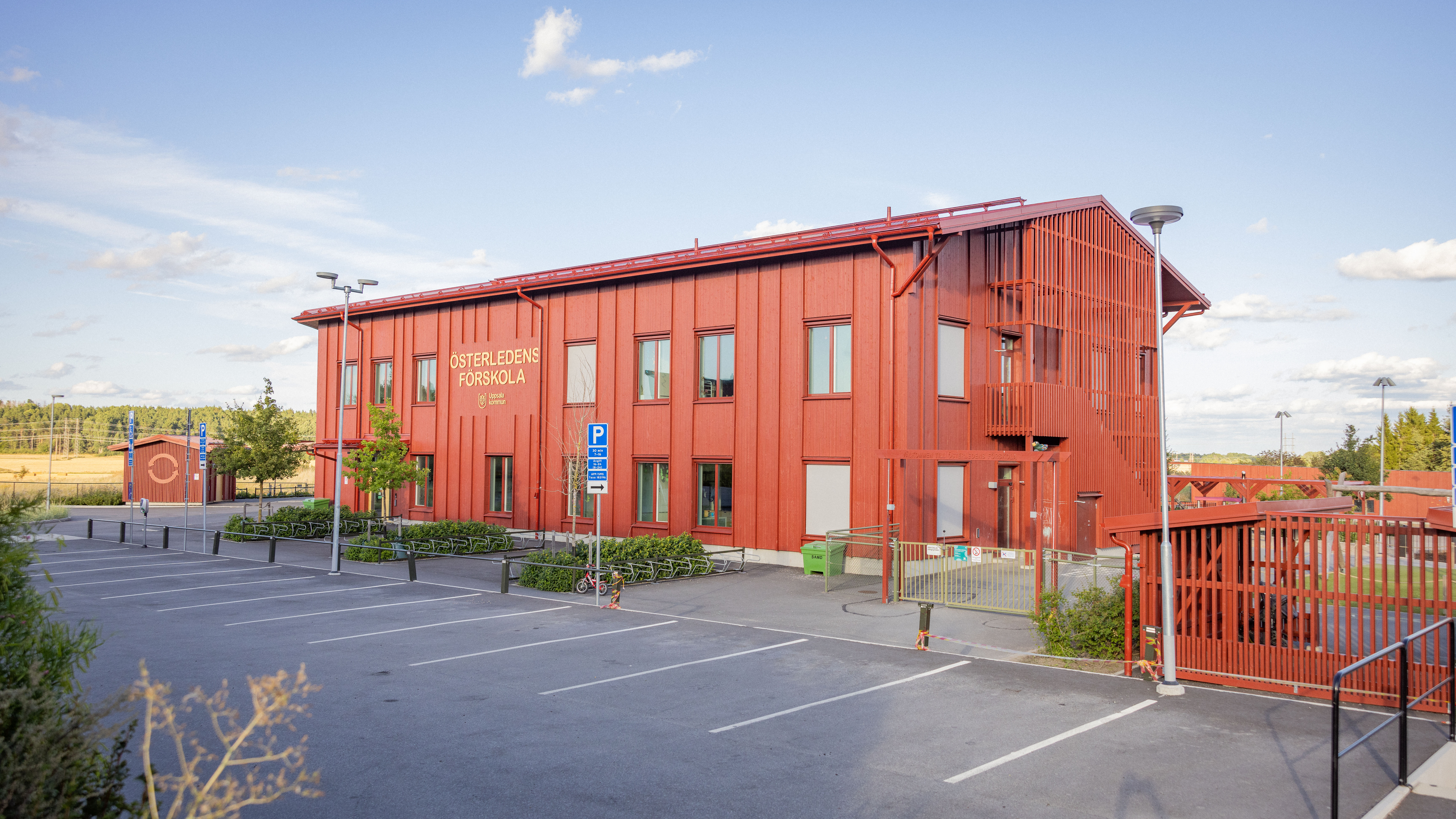 Nybyggd röd förskola i trä med en asfalterad parkering i förgrunden.