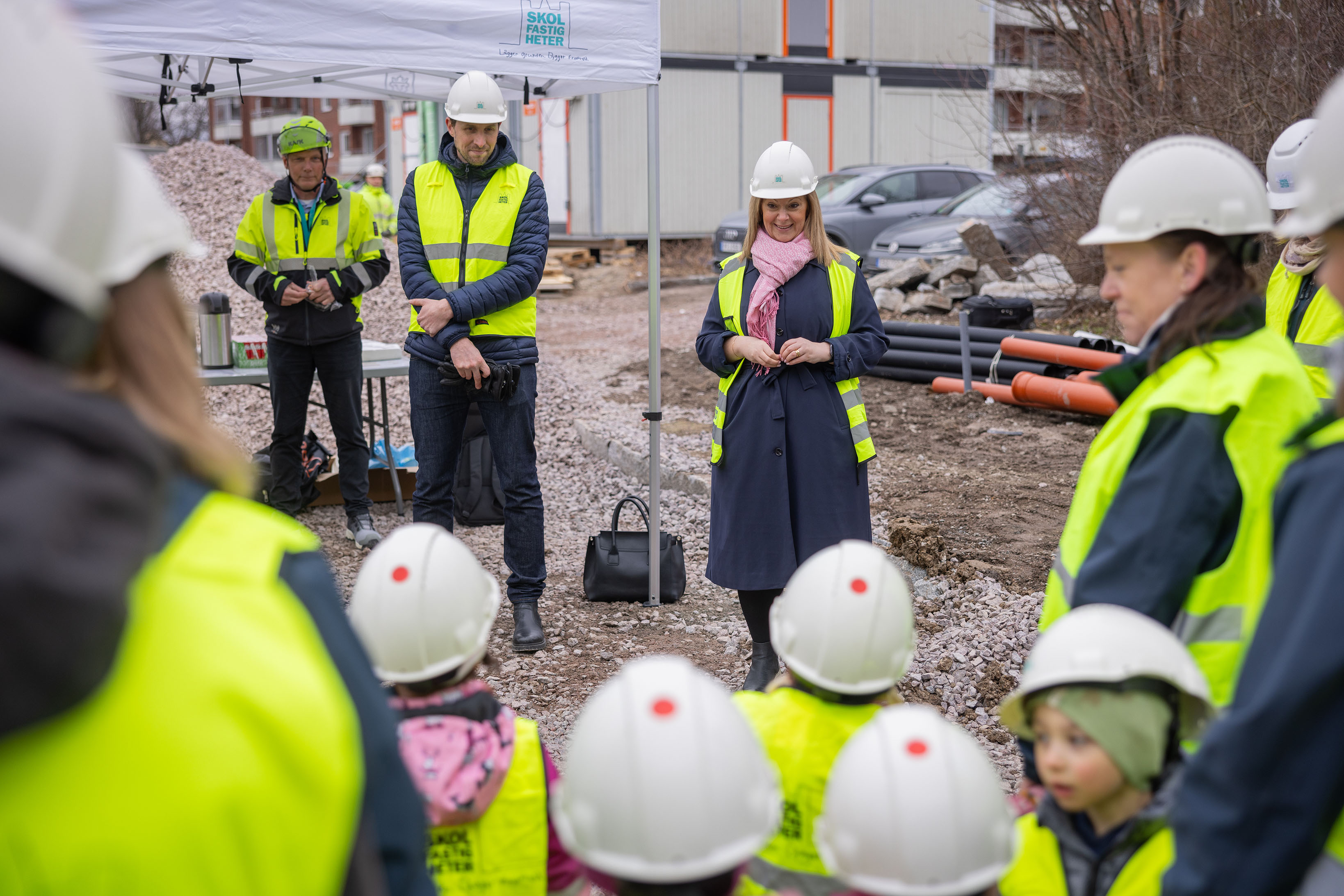En kvinna håller tal inför en grupp människor på en byggplats.