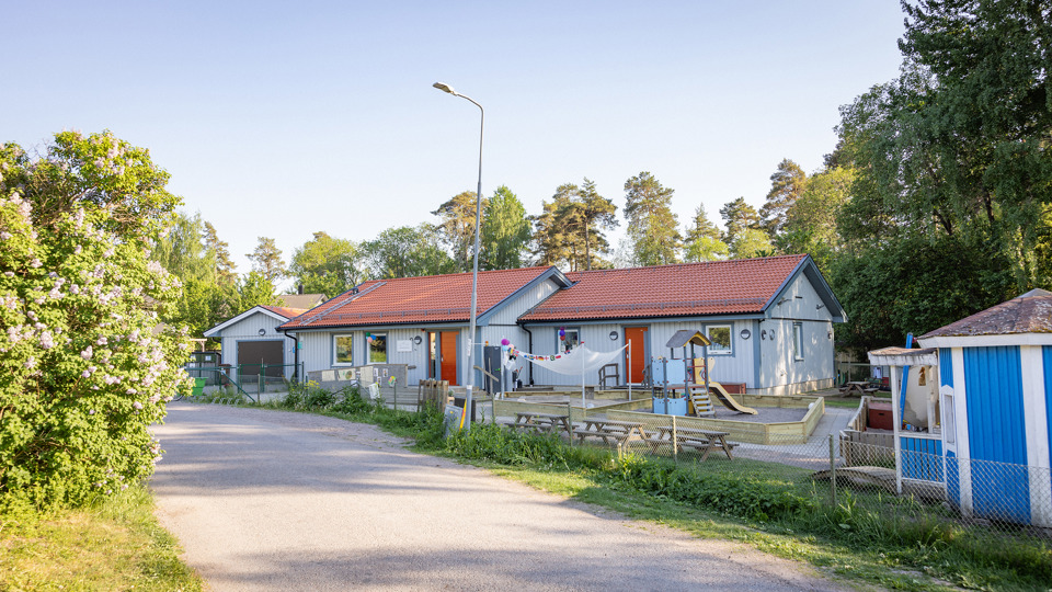 Vit förskola med förskolegård och lekutrustning i förgrunden