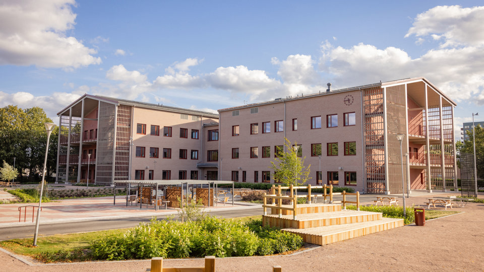 Nya skola med utemiljö och träbänkar sedd på avstånd.