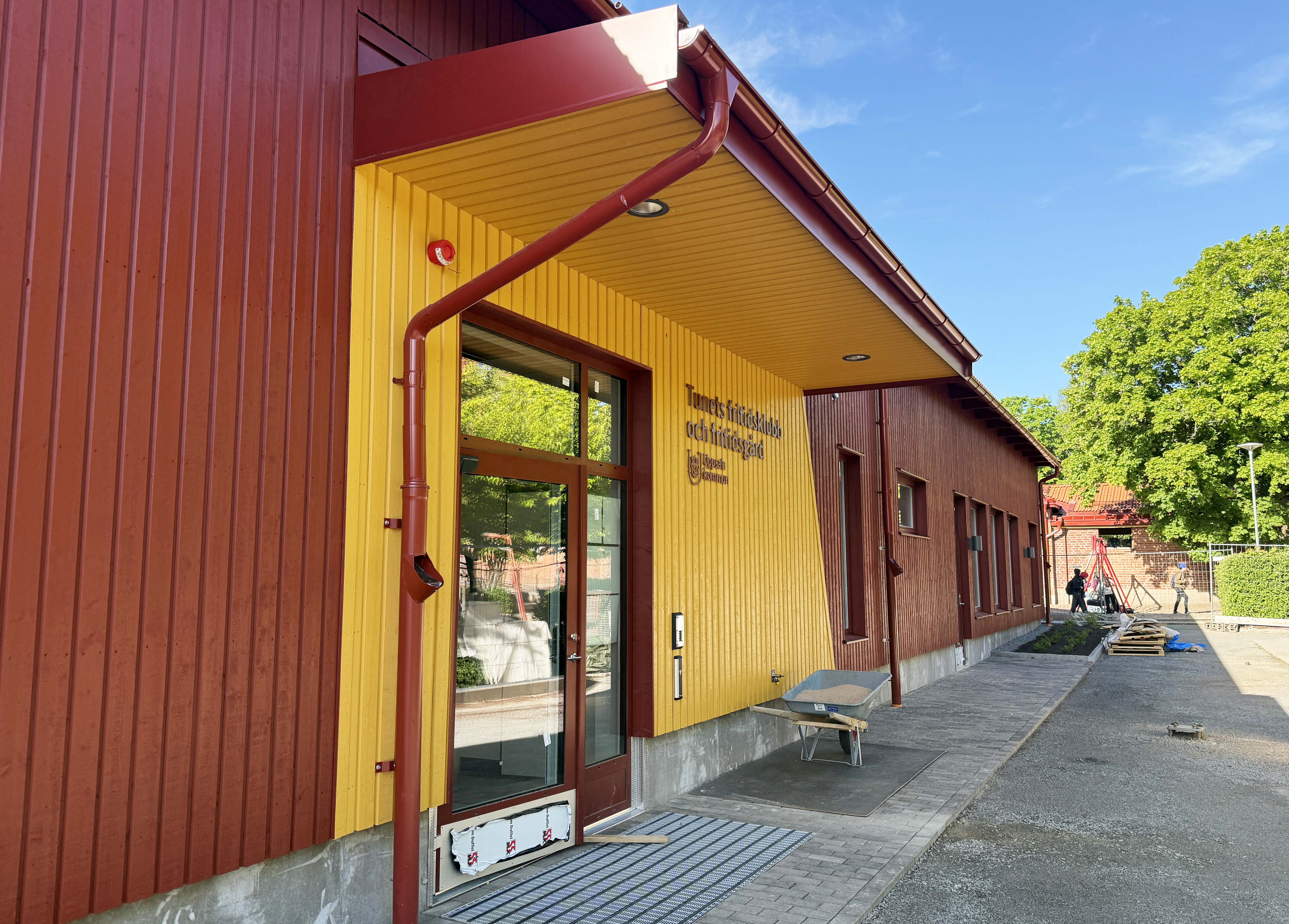 Entre till en nybyggd fritidsklubb med röd och gul träfasad.